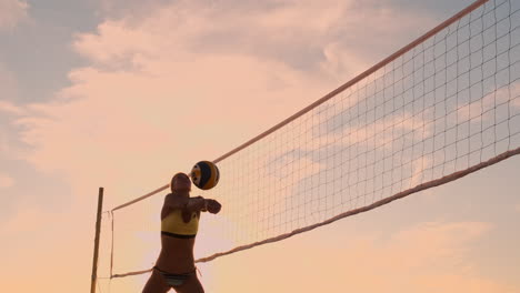 Athletic-girl-playing-beach-volleyball-jumps-in-the-air-and-strikes-the-ball-over-the-net-on-a-beautiful-summer-evening.-Caucasian-woman-score-a-point.